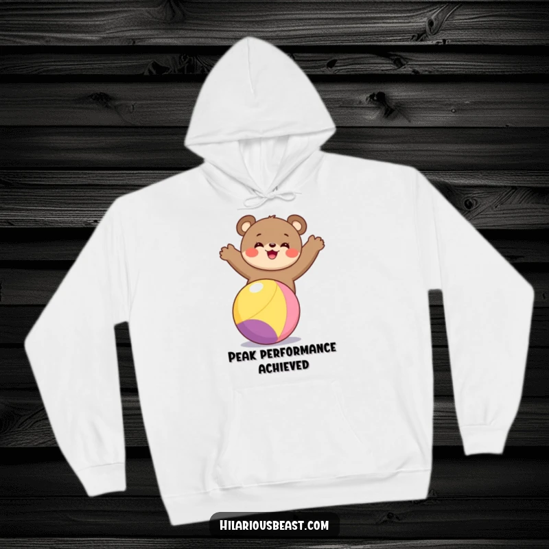 Funny bear cub hoodie showcasing a beaming bear cub masterfully balancing atop a colorful sphere, promising warmth and laughter for the wearer.